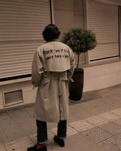 Man wearing beige trench coat with statement text on the back